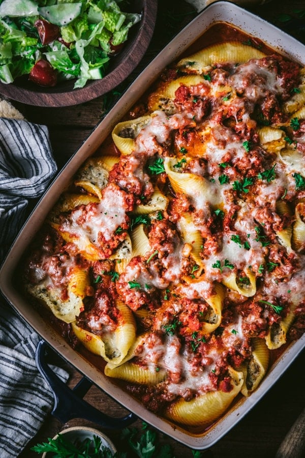 Overhead shot of easy stuffed pasta shells on a wooden dinner table with a salad on the side