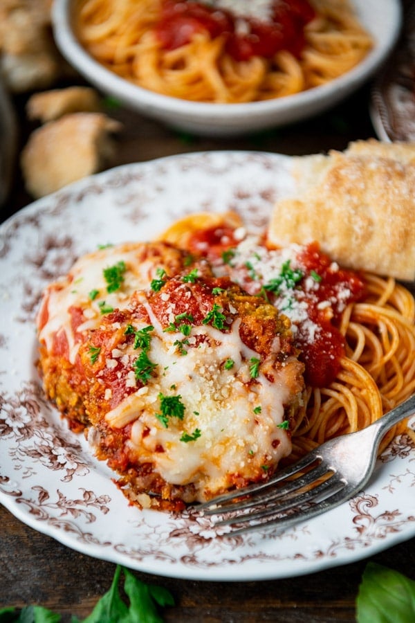 Side shot of eggplant parmesan on a plate with a side of spaghetti.
