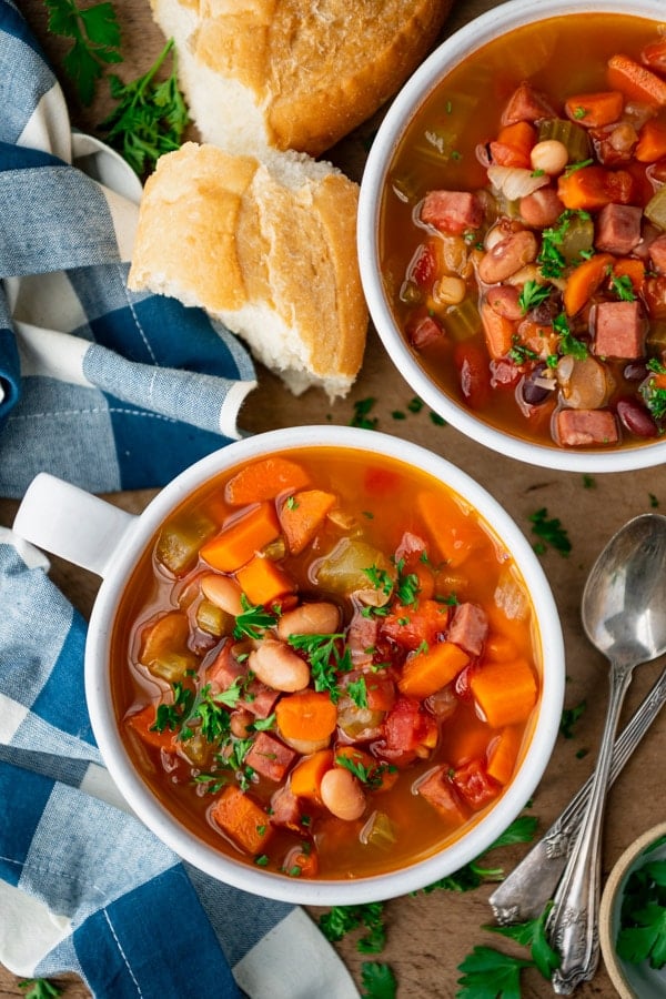 Overhead shot of two bowls of bean soup on a table with French bread on the side