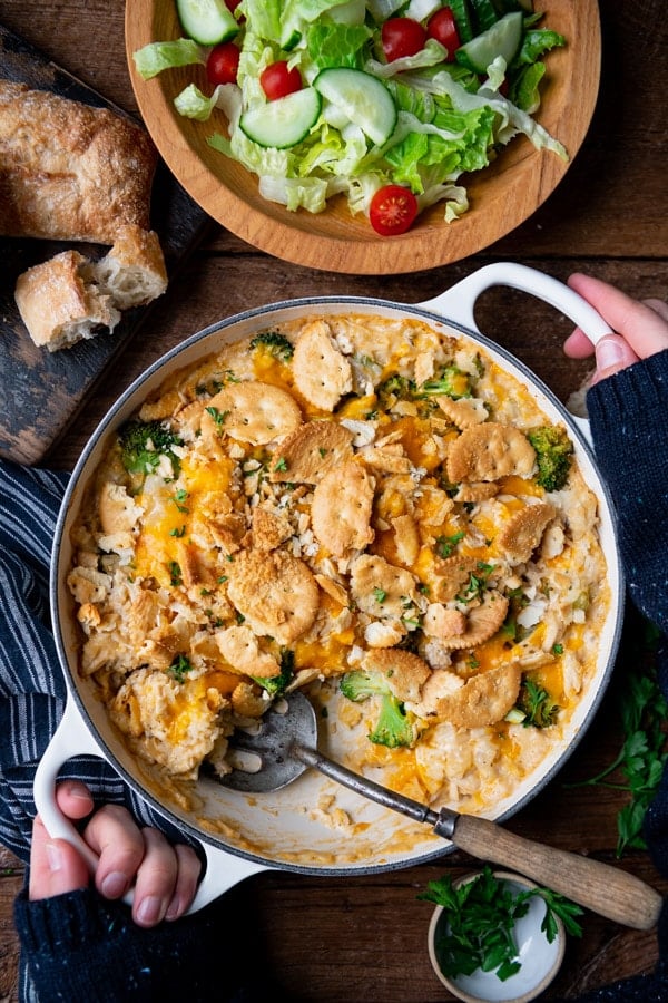 Close overhead shot of hands holding a cheesy chicken broccoli and rice casserole on a wooden table.