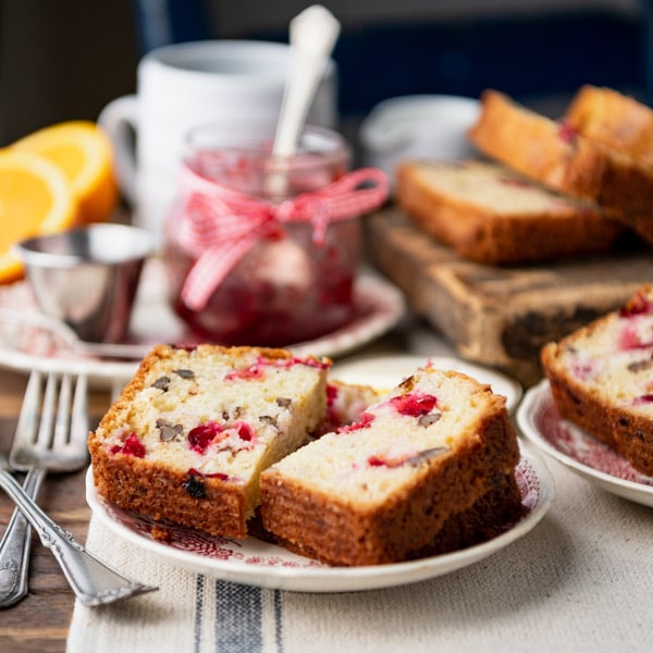 A single slice of cranberry bread, cut in half, and served on a small tea plate with silver forks.