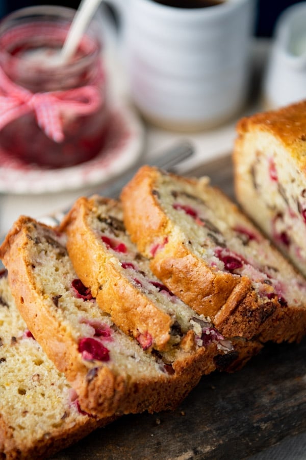 A close up shot of slices of fresh baked cranberry bread, laid out on a wooden cutting board.