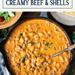 Overhead shot of creamy beef and shells recipe in a cast iron skillet with text title box at top