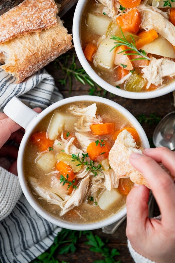Hands dipping bread in a bowl of healthy chicken stew.