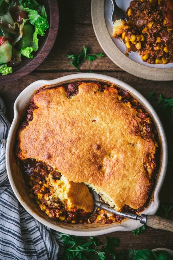 Overhead shot of a ground beef cornbread casserole on a dinner table with a side salad