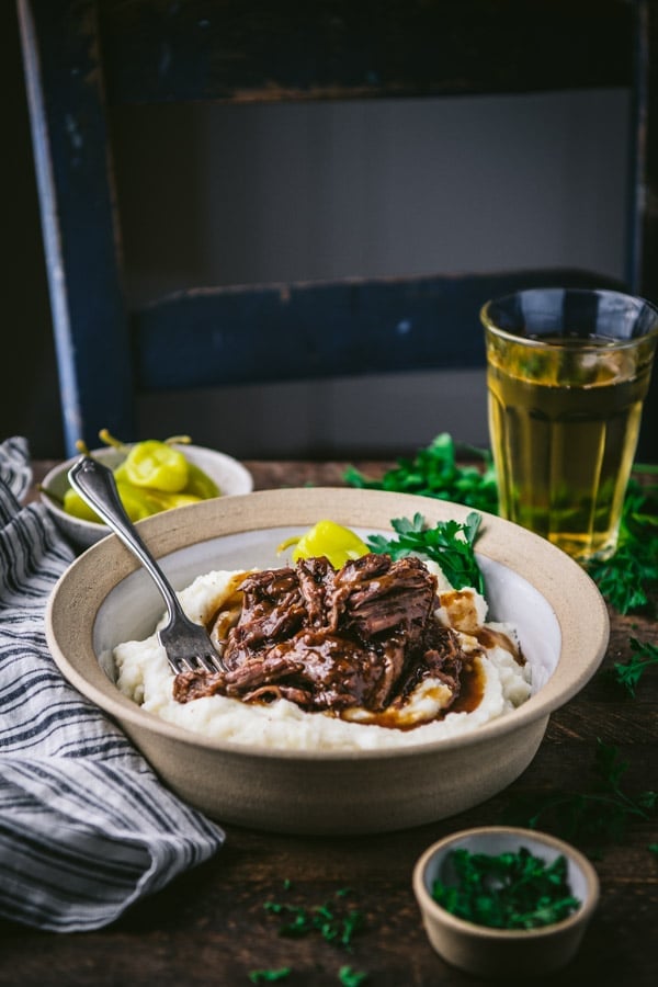 Side shot of a bowl of Mississippi Pot Roast crock pot with mashed potatoes and pepperoncini garnish.