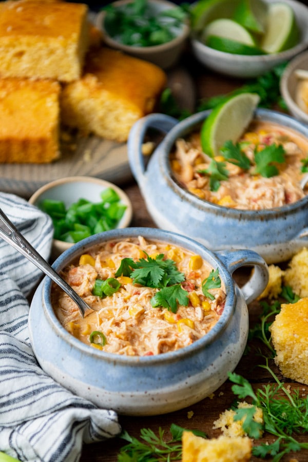 Side shot of cream cheese chicken chili bowls on a table with cornbread