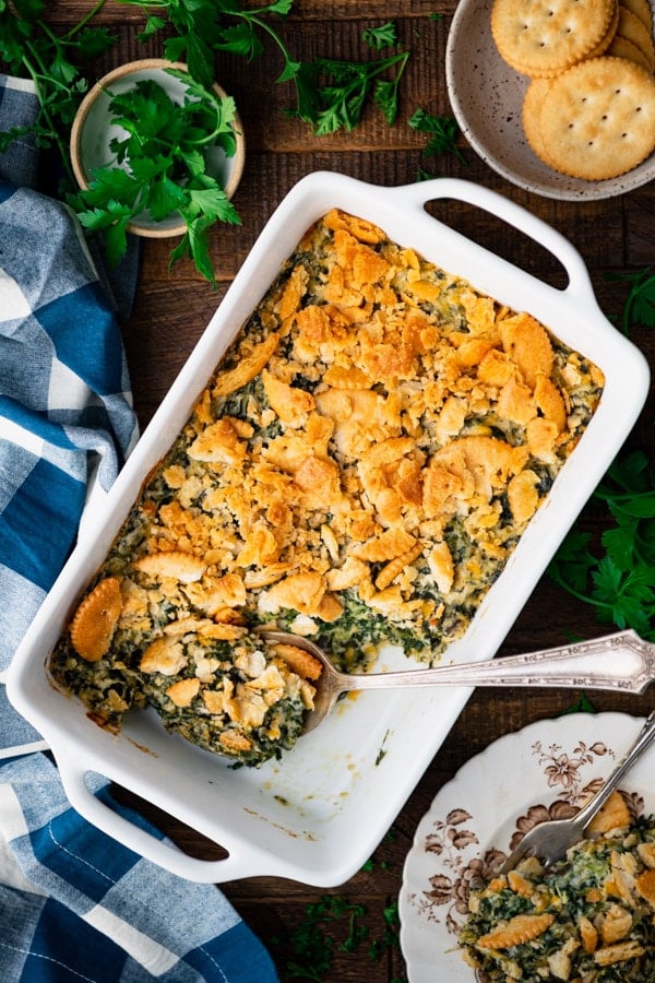 Creamed spinach casserole recipe on a wooden table with a blue and white cloth napkin nearby.