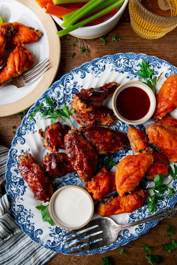 Baked chicken wings, coated with BBQ sauce and buffalo sauce, served on a platter with a side of carrot and celery sticks. Served with glasses of beer.