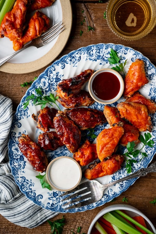 An overhead shot of barbecue and buffalo baked chicken wings on a platter, served with a side of ranch dressing and BBQ sauce.