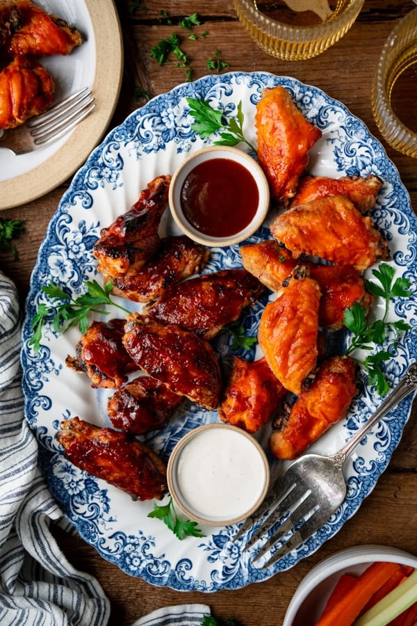 An overhead image of a platter filled with BBQ and buffalo baked chicken wings, served with ranch and BBQ sauce for dipping.
