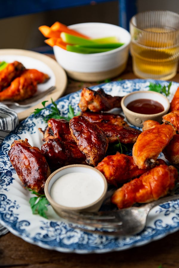 A platter of crispy baked chicken wings coated in BBQ sauce and buffalo sauce. These wings are served with carrots and celery, and ranch and BBQ sauce for dipping.