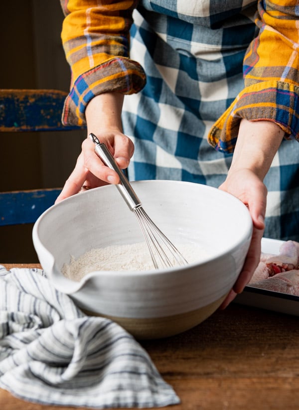 Whisking together seasoned flour in a large white bowl