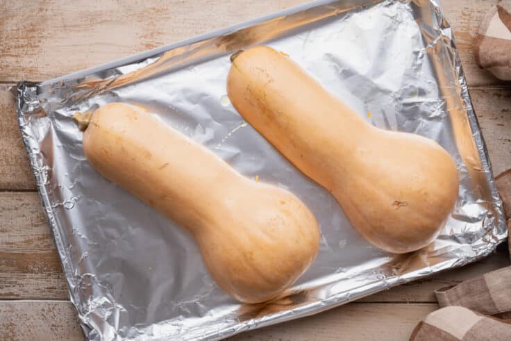 Butternut squash halved and placed cut side down on a sheet pan.