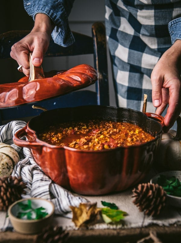 Hands lifting the lid off of a pot of pumpkin chili