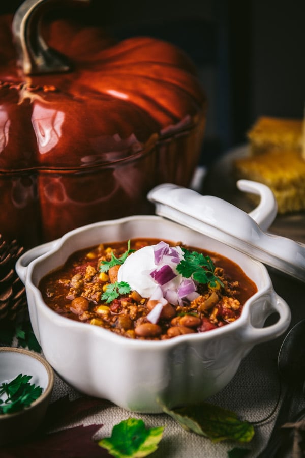 Side shot of pumpkin chili recipe served in a white bowl with toppings on a dinner table