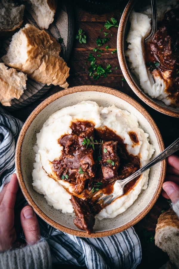 Overhead image of hands holding a bowl of mashed potatoes and braised beef roast.