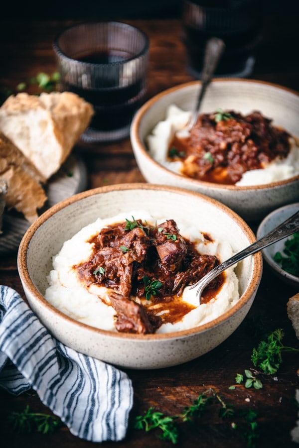 Two bowls of braised beef and potatoes served with red wine and a loaf of bread.