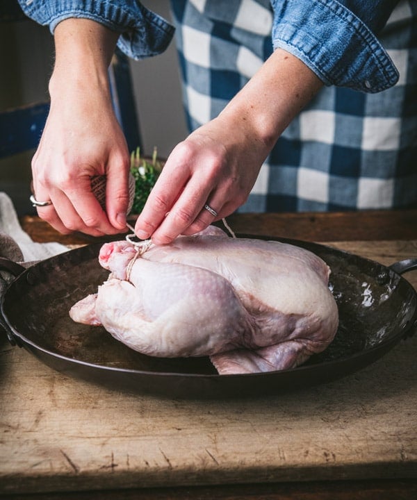 Trussing a chicken in a cast iron pan.