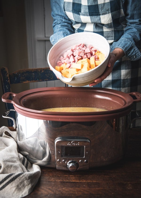 Adding a bowl of ham and cheese to a slow cooker.