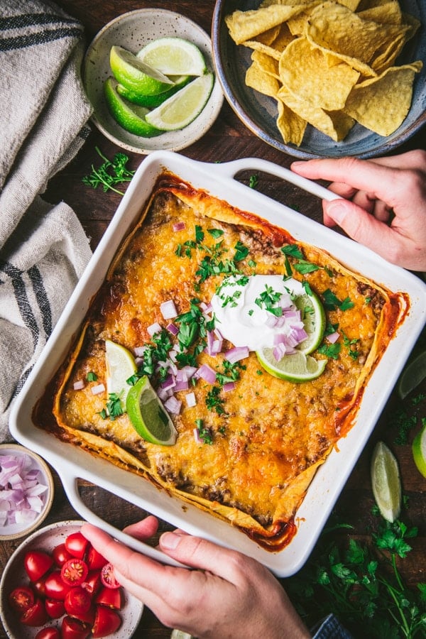 Overhead shot of hands holding a square white dish with easy beef enchilada casserole.