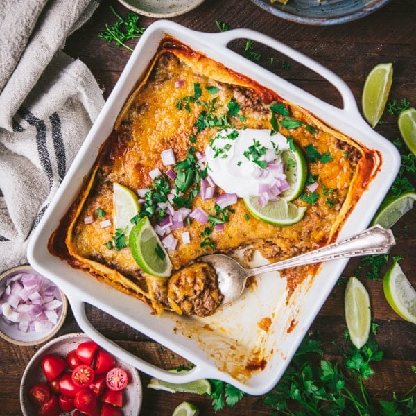 Square overhead image of a white baking dish with beef enchilada casserole.