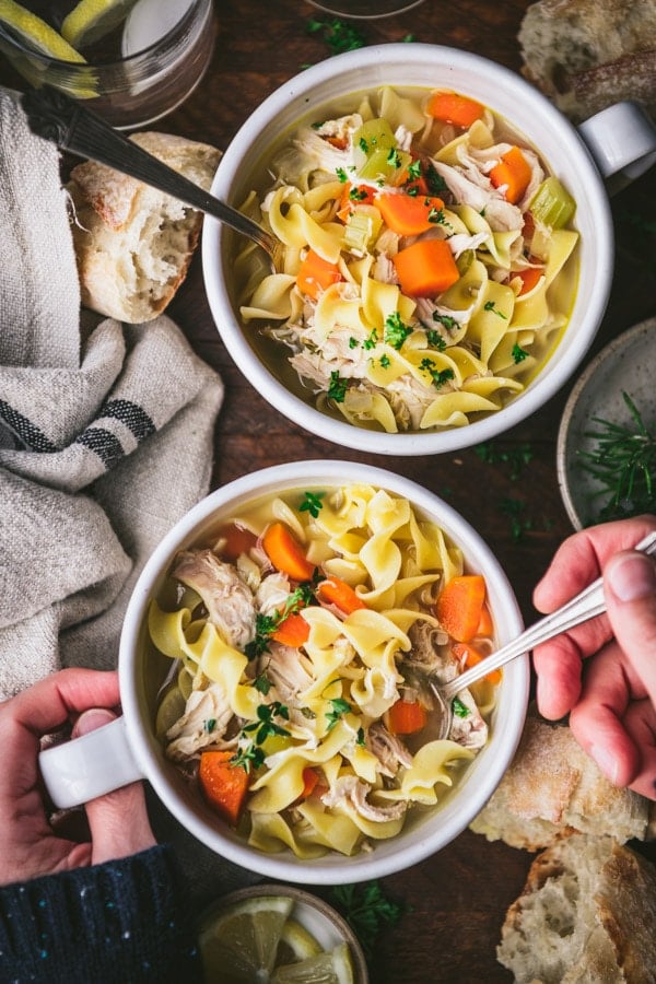 Overhead image of two bowls of easy chicken noodle soup garnished with parsley and thyme on a farmhouse table.