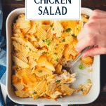 Hands serving hot chicken salad from a white dish with text title overlay.