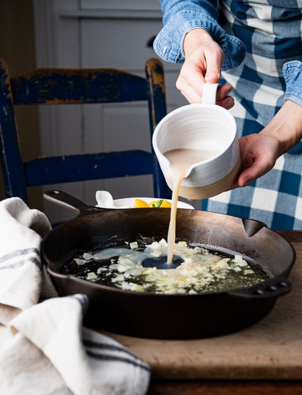 Pouring clam juice and white wine in a cast iron skillet.