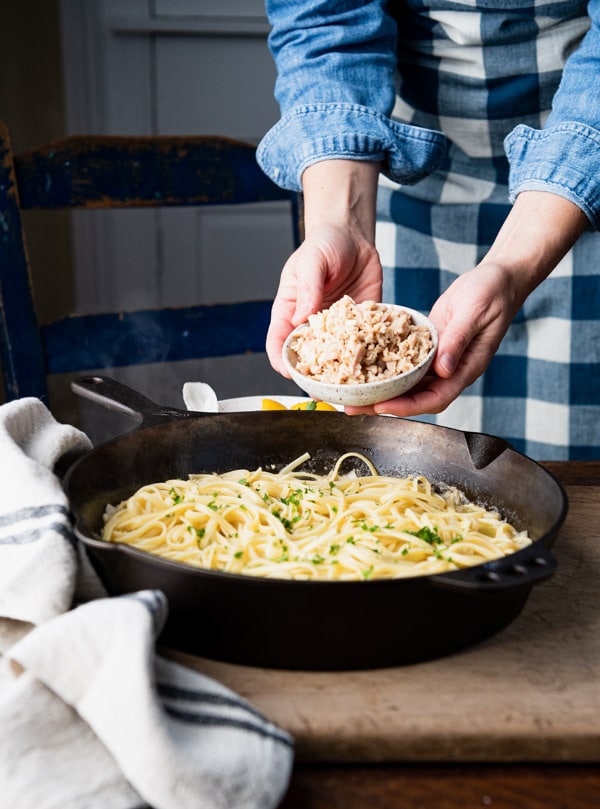 Adding canned chopped clams to a cast iron skillet.