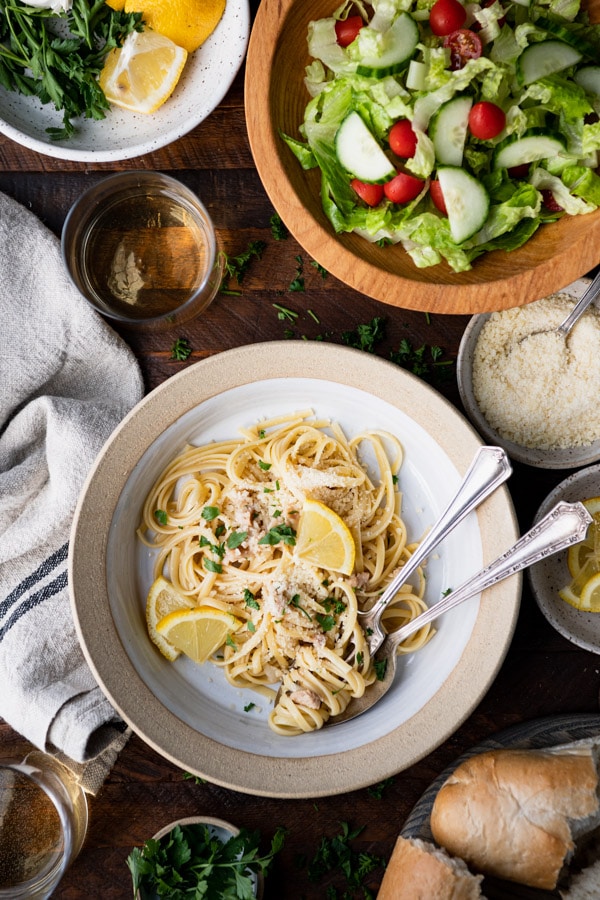 Overhead image of a bowl of linguine with clams in white wine sauce with a side of bread and salad.