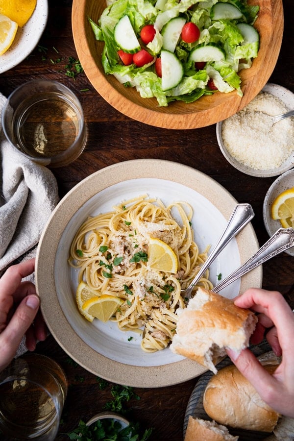 Overhead shot of the best linguine with clam sauce recipe served in a white pasta bowl with a side of bread and salad.