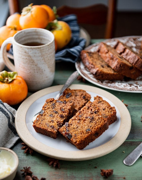 Two slices of persimmon bread cut in half and served on a plate with coffee.