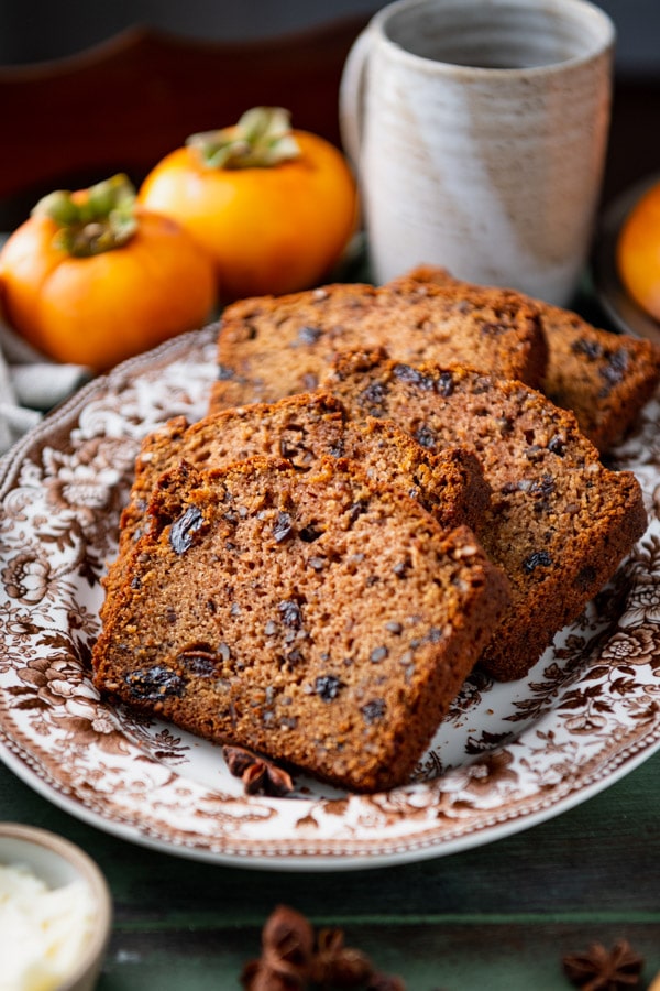A side-angle shot of slices of persimmon bread laid out on a white and brown floral patterned platter.