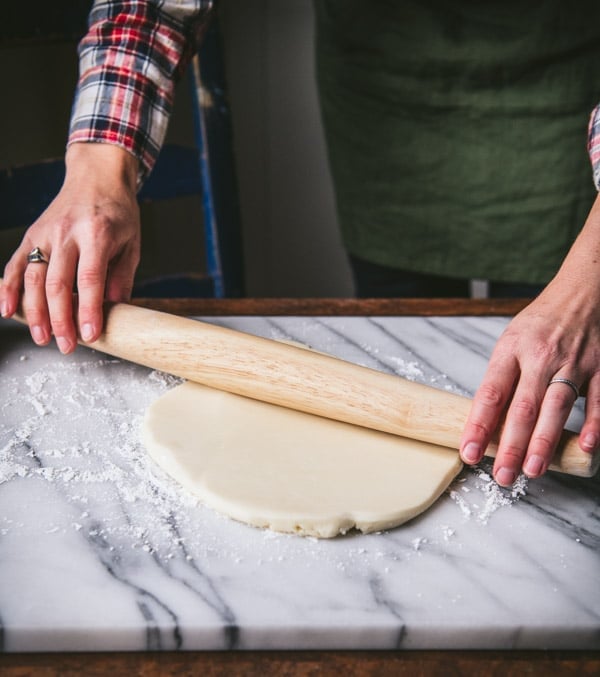 Rolling cookie dough with a wooden rolling pin on a marble board.