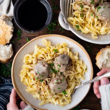 Overhead shot of hands eating Swedish meatballs in a rustic white dish