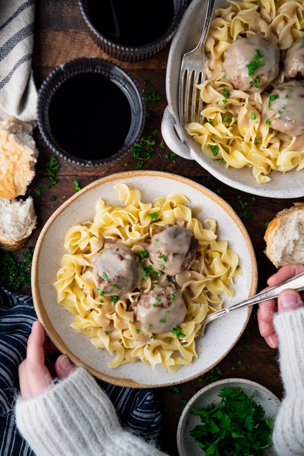 Overhead shot of hands eating Swedish meatballs in a rustic white dish