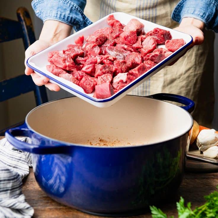 Adding beef to a Dutch oven for a beef burgundy recipe.