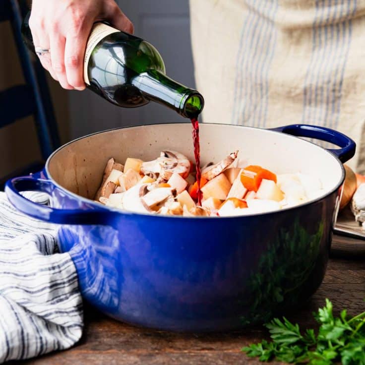 Pouring red wine into a cast iron Dutch oven.