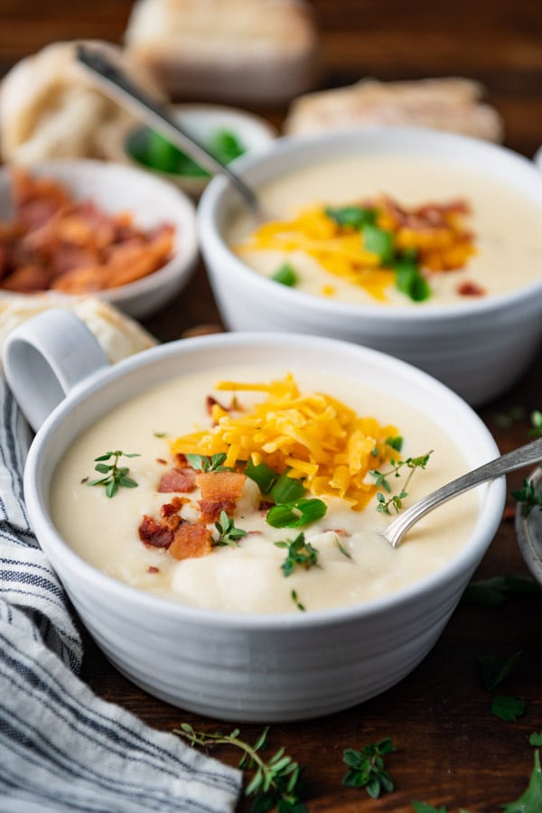 Close side shot of bowls of crockpot potato soup on a dinner table.