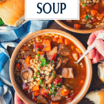Overhead image of hands eating a bowl of beef barley soup with text title overlay