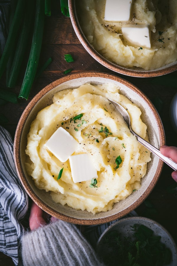 Overhead shot of hands serving a bowl of creamy buttermilk mashed potatoes.