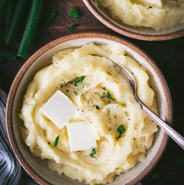 Close overhead image of two bowls of buttermilk mashed potatoes on a dinner table.