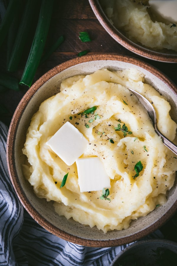 Close overhead shot of a bowl of the best mashed potatoes in a bowl with fresh herbs and butter on top.
