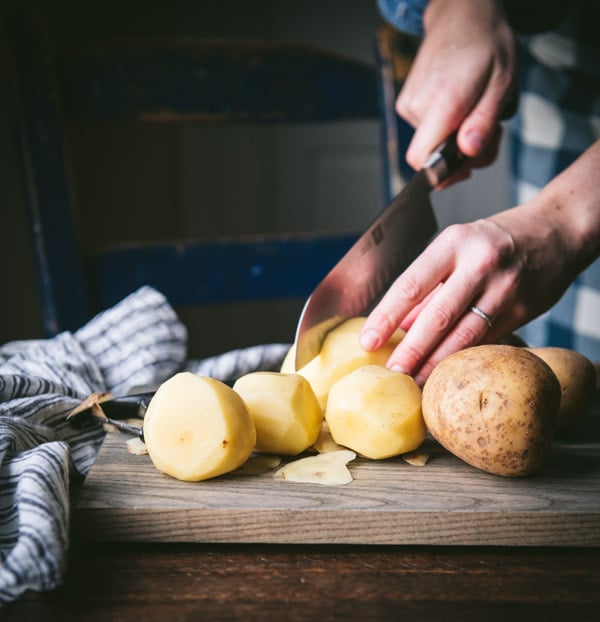 Peeling and cutting Yukon Gold potatoes on a cutting board.