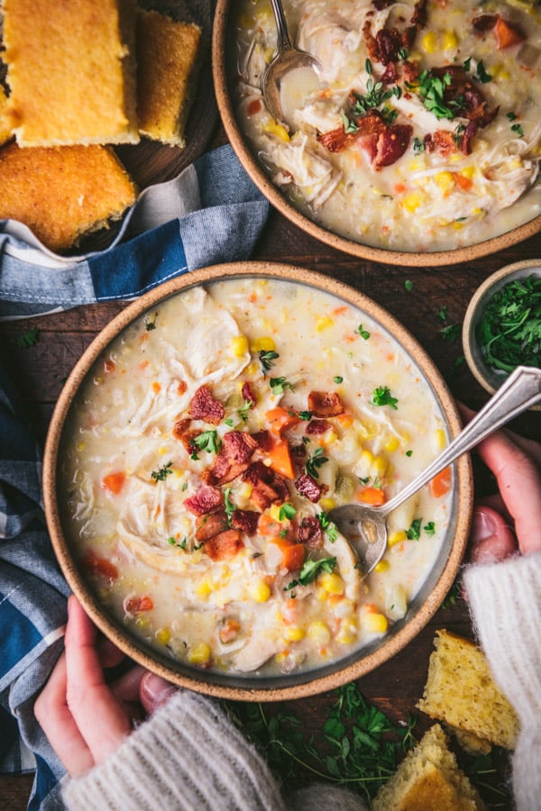 Hands holding slow cooker chicken corn chowder recipe with a side of cornbread