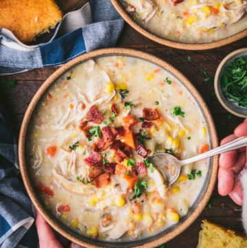 Overhead image of hands eating a bowl of chicken and corn chowder with crispy bacon on top