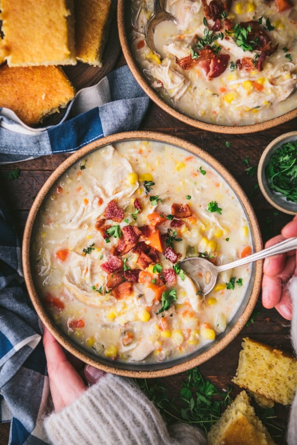 Aerial image of hands eating a bowl of chicken and corn soup with crispy bacon on top