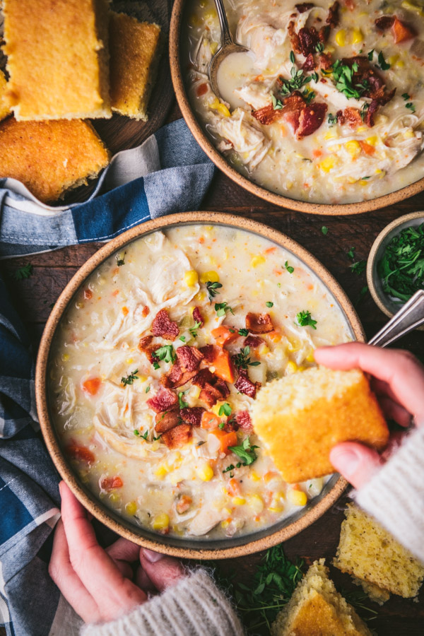 Hands dipping cornbread into a bowl of chicken corn chowder