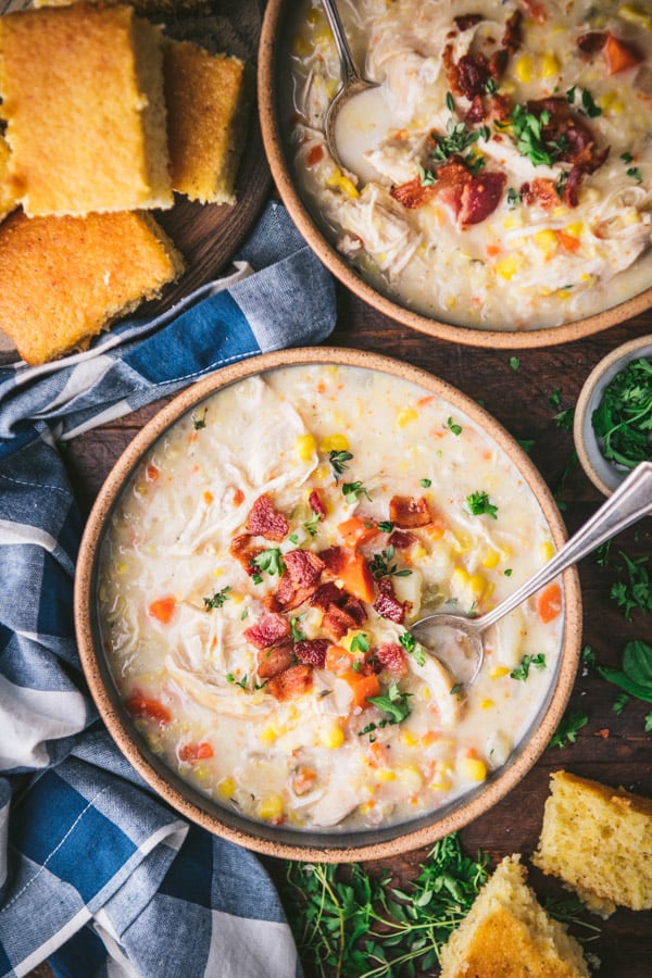 Aerial shot of two bowls of chicken corn soup with bacon and one side of cornbread